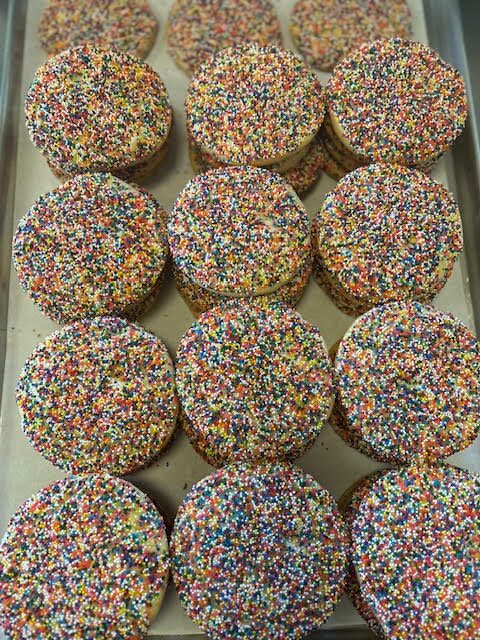 Colorful sprinkle-covered cookies stacked neatly on a tray.